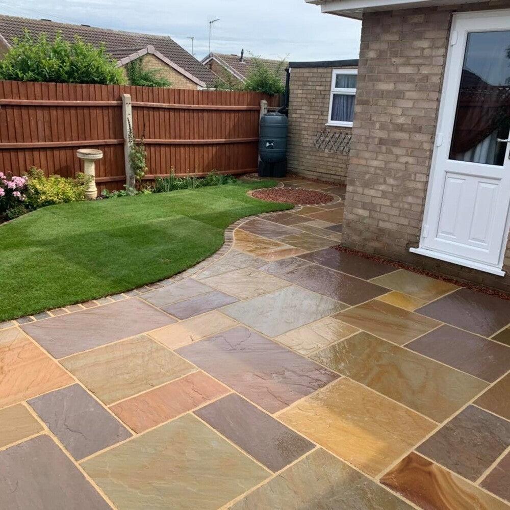 Natural sandstone patio flowing around a freshly laid lawn